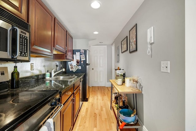 kitchen featuring appliances with stainless steel finishes, light wood-type flooring, a sink, dark stone counters, and recessed lighting
