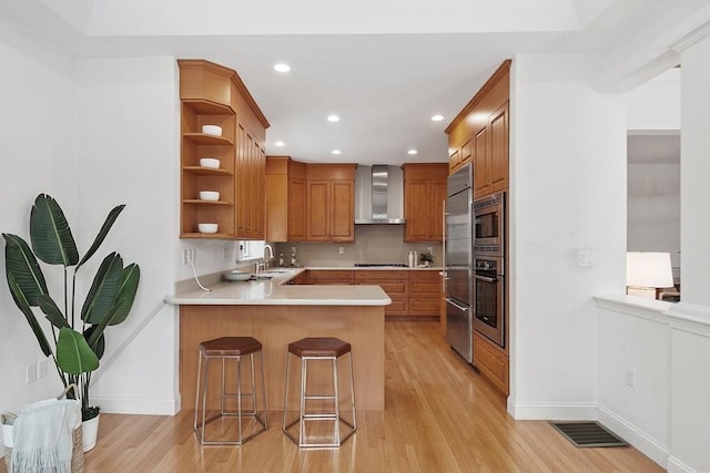 kitchen featuring light countertops, appliances with stainless steel finishes, a sink, a peninsula, and wall chimney exhaust hood