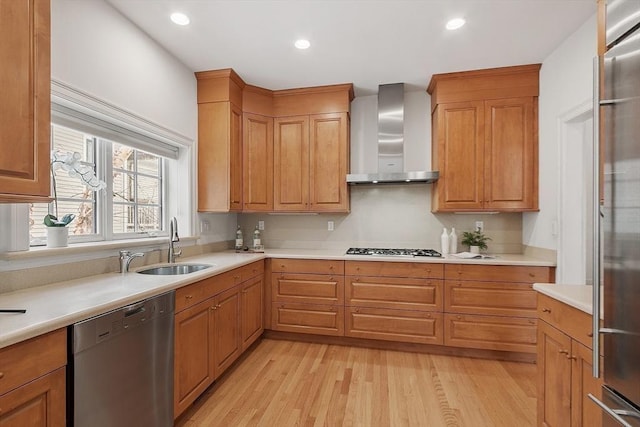 kitchen featuring stainless steel appliances, light countertops, light wood-style flooring, a sink, and wall chimney exhaust hood