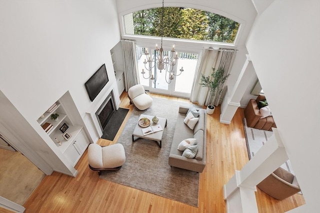 living room featuring built in features, a towering ceiling, a fireplace with flush hearth, light wood-style floors, and a notable chandelier