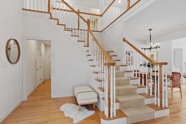 stairs with a notable chandelier, a towering ceiling, baseboards, and wood finished floors