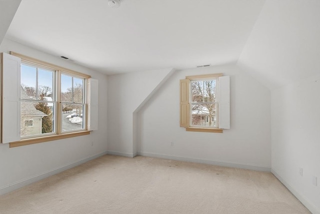 additional living space with light carpet, vaulted ceiling, visible vents, and baseboards