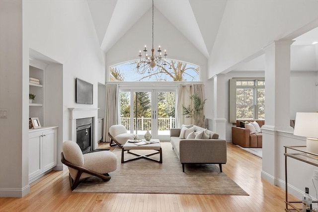 interior space with built in shelves, a glass covered fireplace, decorative columns, and light wood finished floors