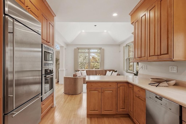 kitchen with light wood-style flooring, light countertops, a peninsula, and built in appliances