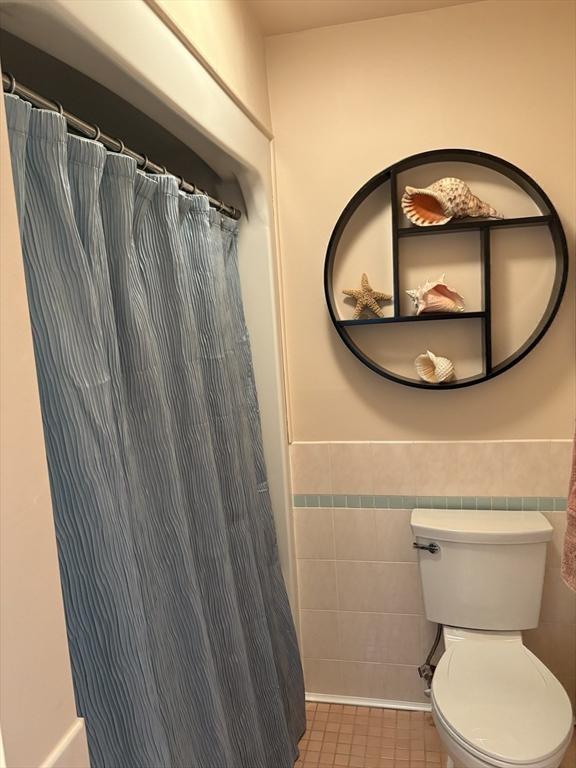 bathroom with tile patterned floors, toilet, curtained shower, and tile walls