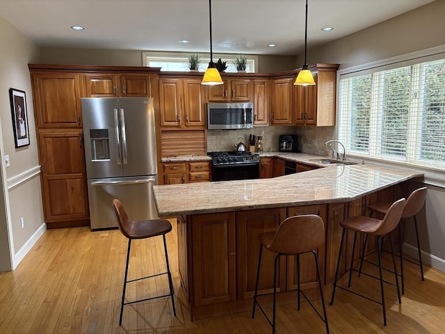 kitchen featuring sink, a breakfast bar, appliances with stainless steel finishes, hanging light fixtures, and light stone counters