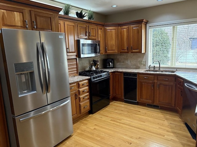 kitchen with sink, light stone counters, appliances with stainless steel finishes, light hardwood / wood-style floors, and decorative backsplash