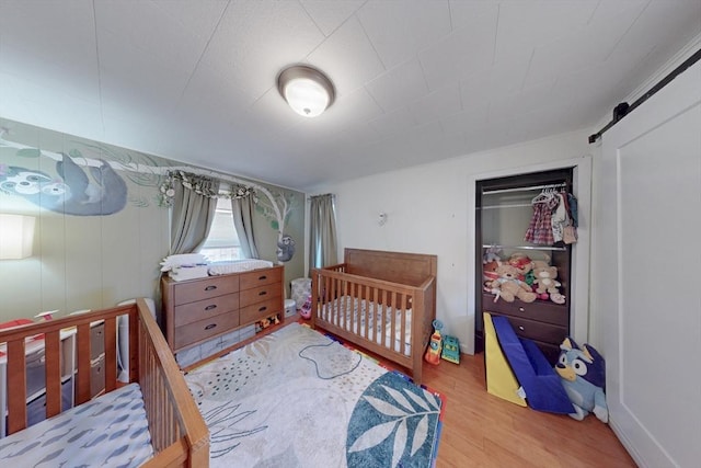 bedroom featuring light wood-style flooring, a nursery area, a closet, and a barn door