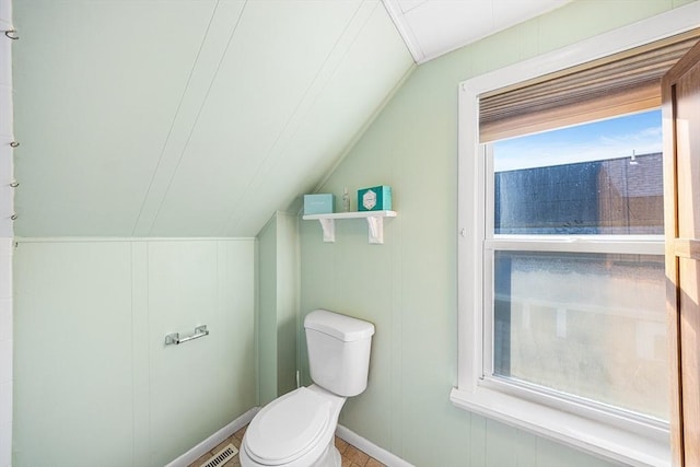 bathroom featuring lofted ceiling, toilet, and a decorative wall