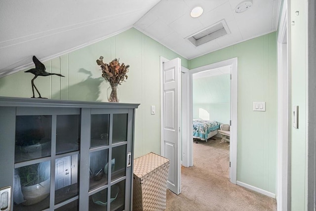 hallway featuring vaulted ceiling, light carpet, and a decorative wall