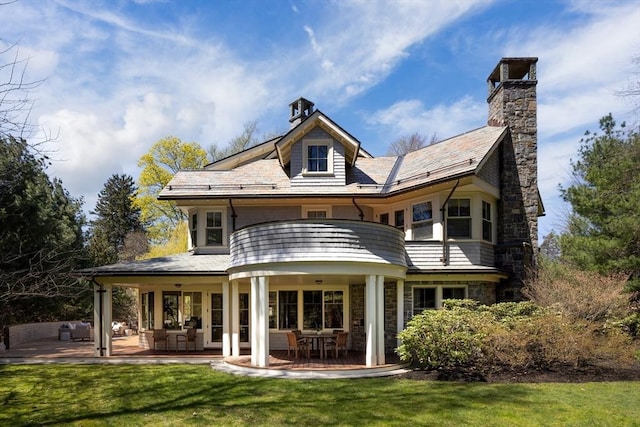 back of house with a patio, a yard, a chimney, and stone siding