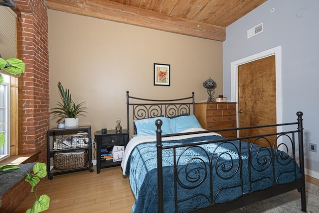 bedroom featuring beam ceiling, light hardwood / wood-style flooring, and wooden ceiling