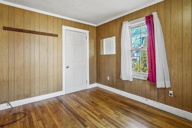 empty room featuring a healthy amount of sunlight, wooden walls, crown molding, and hardwood / wood-style flooring