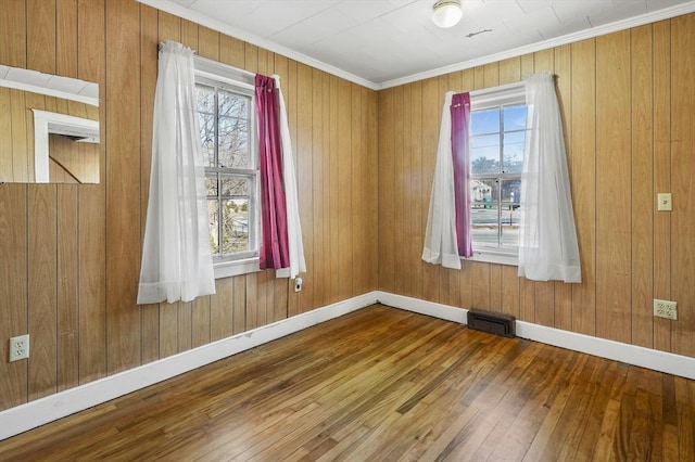 empty room with hardwood / wood-style floors, a wealth of natural light, and crown molding