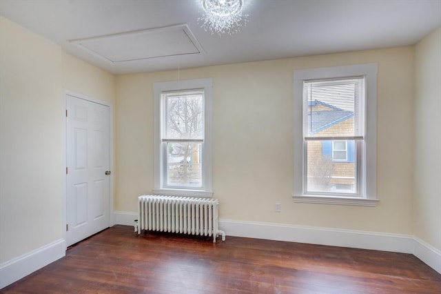 unfurnished room with baseboards, wood finished floors, attic access, and radiator