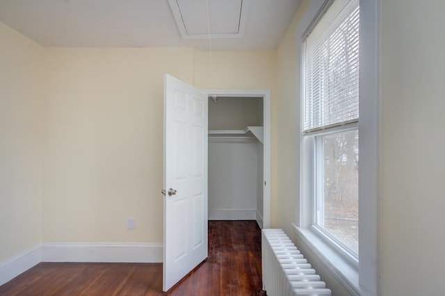 unfurnished bedroom with radiator heating unit, wood finished floors, attic access, and baseboards
