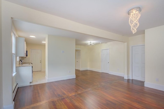 spare room with a baseboard radiator, wood finished floors, baseboards, and an inviting chandelier