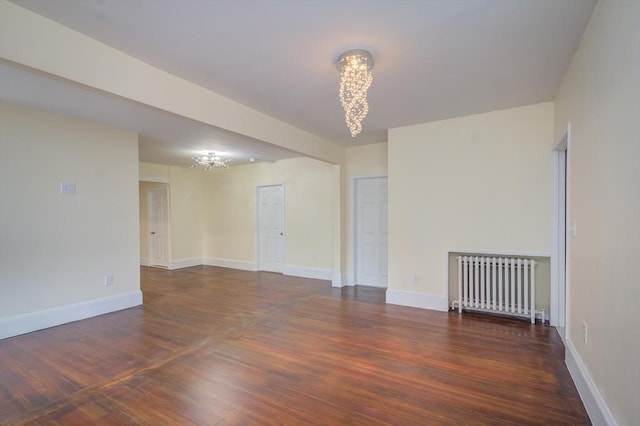 spare room with radiator, a notable chandelier, baseboards, and wood finished floors