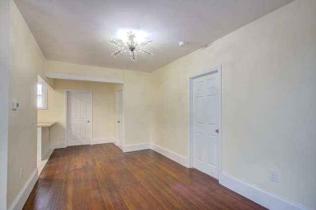 unfurnished room with dark wood-style floors, baseboards, and a notable chandelier