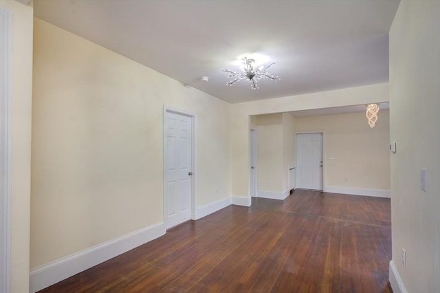 empty room featuring dark wood-style floors, a notable chandelier, and baseboards
