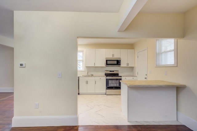 kitchen with baseboards, appliances with stainless steel finishes, a peninsula, light countertops, and white cabinetry