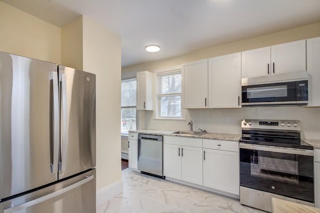 kitchen featuring marble finish floor, appliances with stainless steel finishes, white cabinets, and a sink