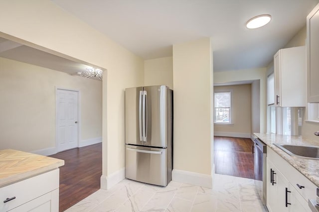 kitchen featuring light stone counters, a sink, baseboards, white cabinets, and appliances with stainless steel finishes