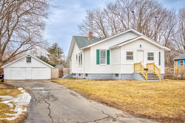 view of front of property with an outbuilding, a detached garage, roof with shingles, a chimney, and a front yard