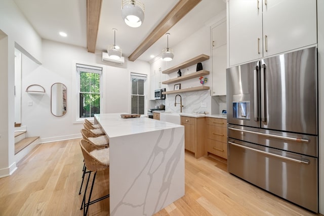 kitchen with appliances with stainless steel finishes, light wood-type flooring, a kitchen island, white cabinetry, and beamed ceiling