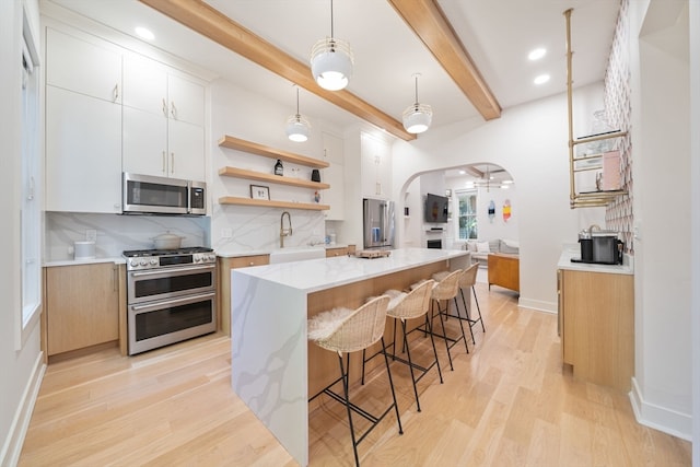 kitchen with appliances with stainless steel finishes, light wood-type flooring, a center island, white cabinetry, and beamed ceiling