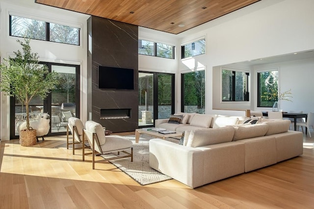 living room with a towering ceiling, light hardwood / wood-style flooring, wooden ceiling, and a premium fireplace