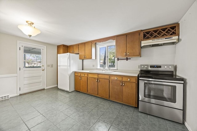 kitchen featuring stainless steel range with electric stovetop, freestanding refrigerator, under cabinet range hood, brown cabinetry, and light countertops
