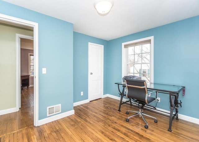 home office with wood finished floors, visible vents, and baseboards