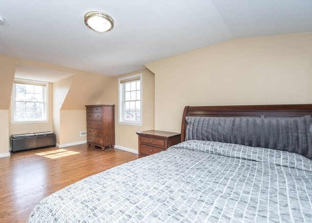 bedroom featuring multiple windows, baseboards, lofted ceiling, and wood finished floors