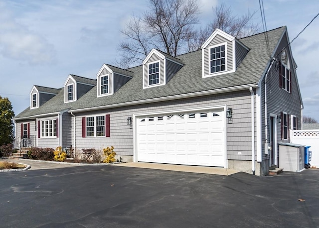 new england style home with aphalt driveway, an attached garage, fence, and roof with shingles