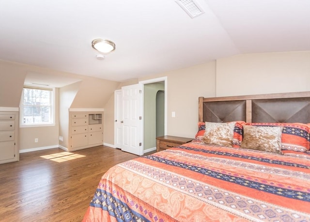 bedroom with wood finished floors, baseboards, visible vents, arched walkways, and vaulted ceiling