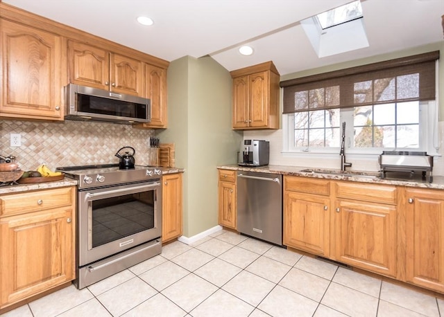 kitchen featuring light stone counters, a skylight, a sink, stainless steel appliances, and tasteful backsplash