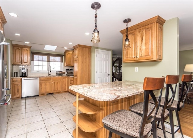 kitchen featuring light stone countertops, a breakfast bar, a peninsula, stainless steel dishwasher, and a sink