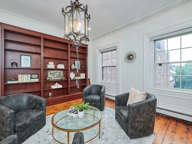 living area with a chandelier, hardwood / wood-style flooring, a baseboard radiator, and crown molding