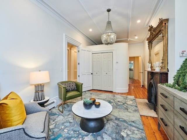 living area with lofted ceiling, a baseboard heating unit, crown molding, light hardwood / wood-style flooring, and a chandelier