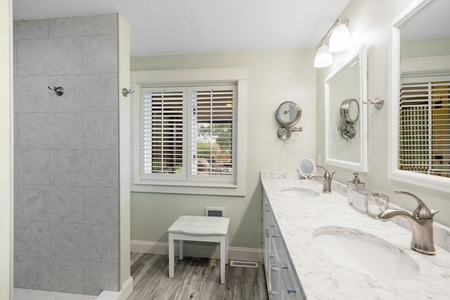 full bath featuring a tile shower, wood finished floors, baseboards, and a sink