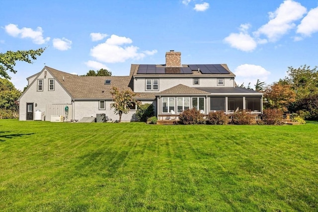 rear view of house featuring solar panels, a lawn, a sunroom, and a chimney