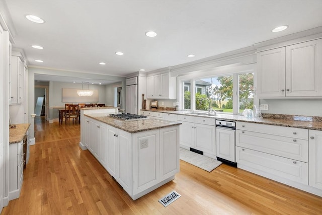 kitchen with light wood finished floors, a center island, stainless steel gas stovetop, white cabinets, and a sink