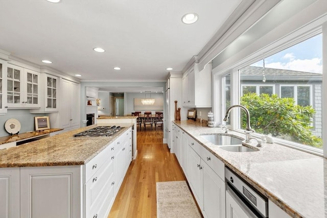 kitchen with a center island, dishwasher, light wood-type flooring, stainless steel gas stovetop, and a sink