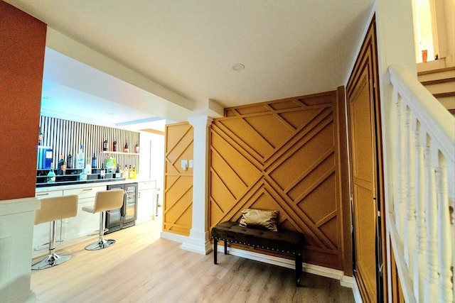 interior space featuring beverage cooler, stairway, decorative columns, and light wood-style floors