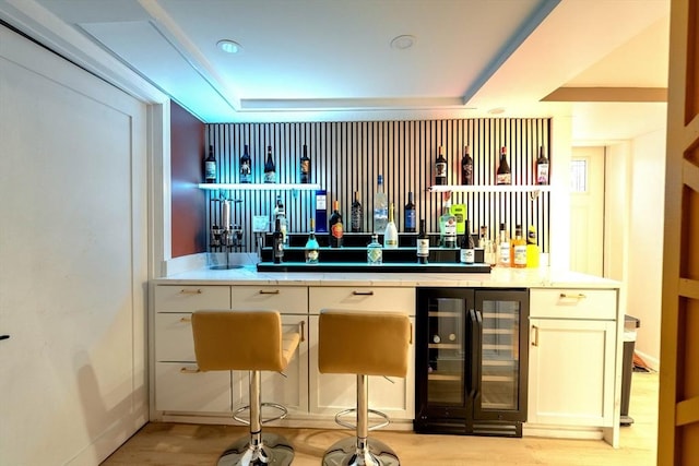 bar featuring light wood-style flooring, a raised ceiling, wet bar, and beverage cooler