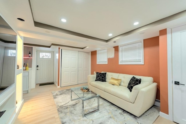 living room with a baseboard heating unit, baseboards, light wood-type flooring, recessed lighting, and a raised ceiling