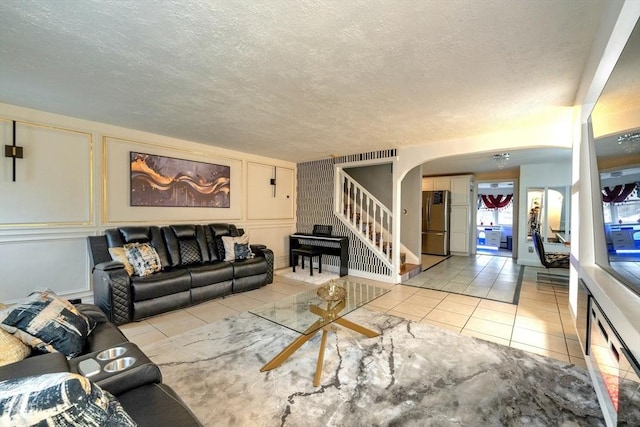 living room featuring a textured ceiling, stairway, arched walkways, a decorative wall, and light tile patterned floors