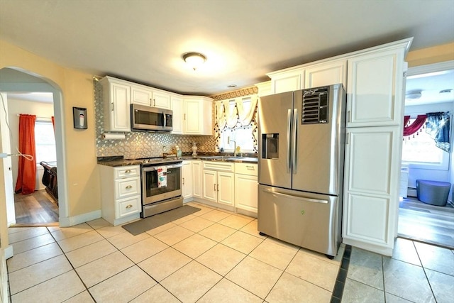 kitchen featuring arched walkways, dark countertops, appliances with stainless steel finishes, and light tile patterned flooring