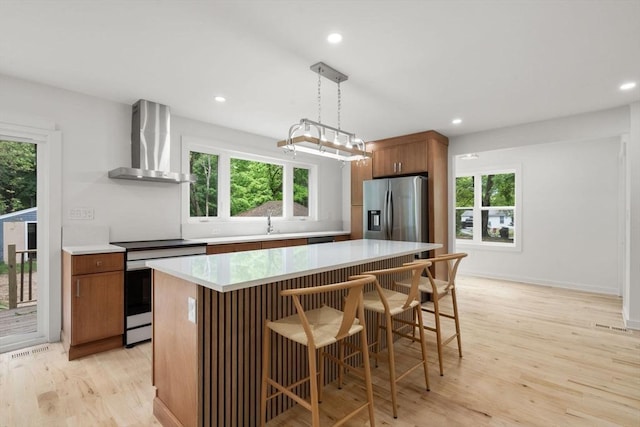 174 Gilbert St, Mansfield, MA 02048 - kitchen featuring wall chimney range hood, appliances with stainless steel finishes, light wood-type flooring, a center island, and light countertops